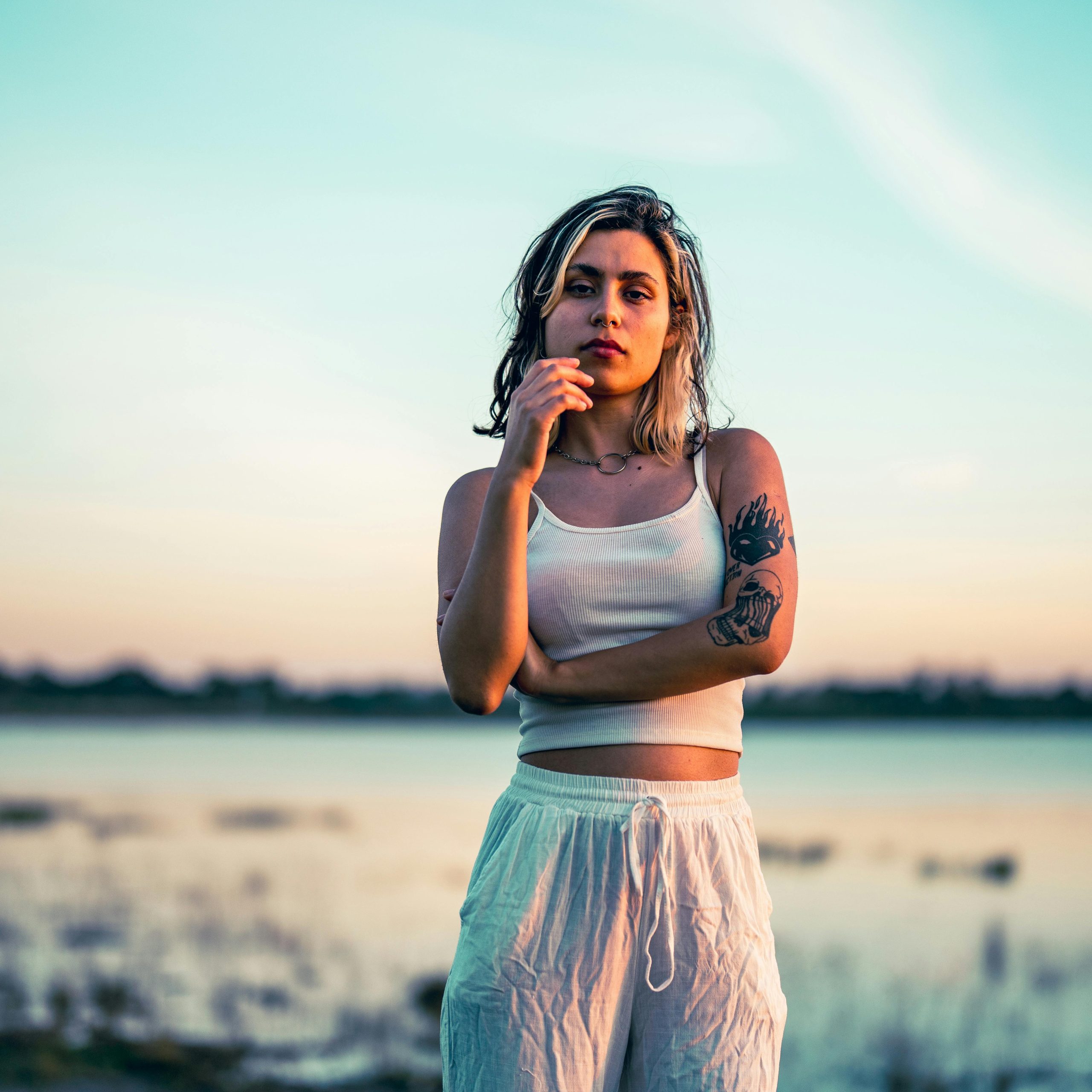 A serene portrait of a tattooed woman standing by the lake during a vibrant sunset in Chascomús, Argentina.