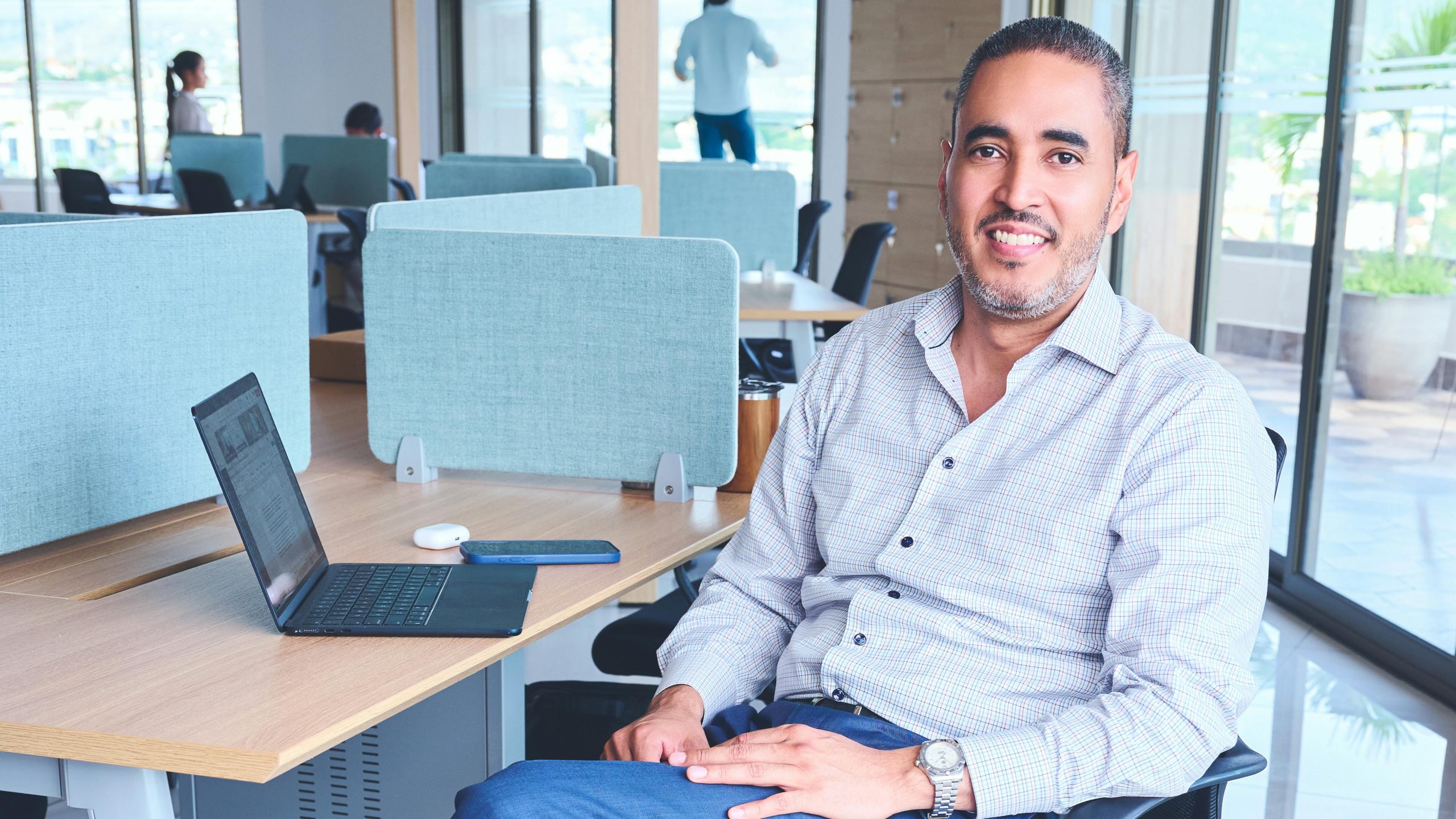 Smiling man sitting at workstation in modern office with laptop.