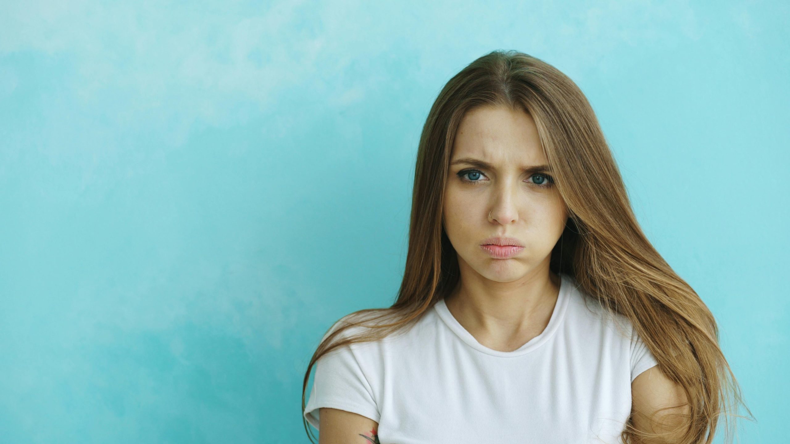 Thoughtful young woman with long hair against a blue background, expressing contemplation.