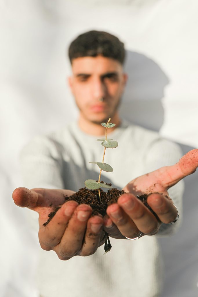 Young man focusing on a sapling, symbolizing growth and environmental care.