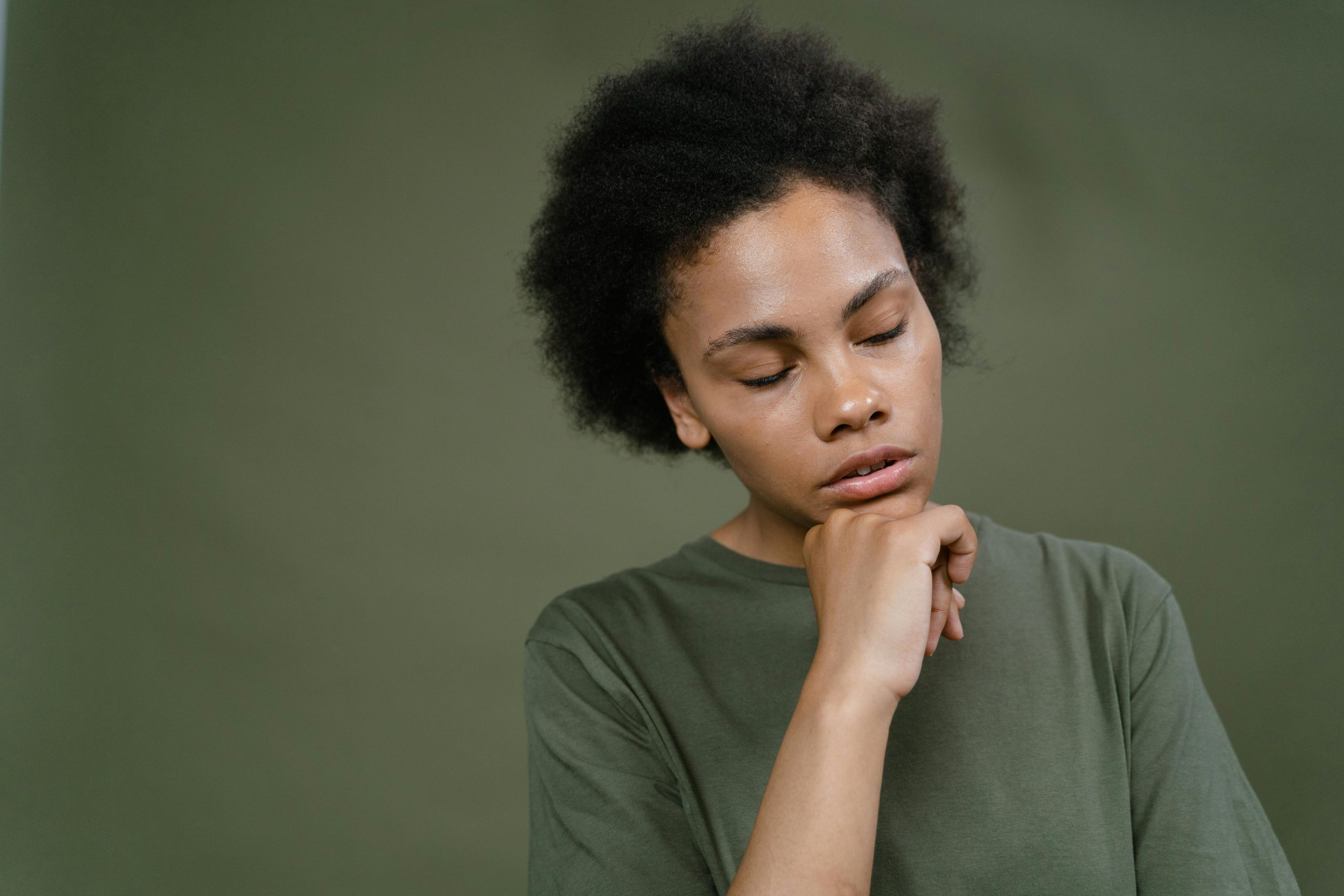 Thoughtful woman with afro hair, hand on chin, in green setting.