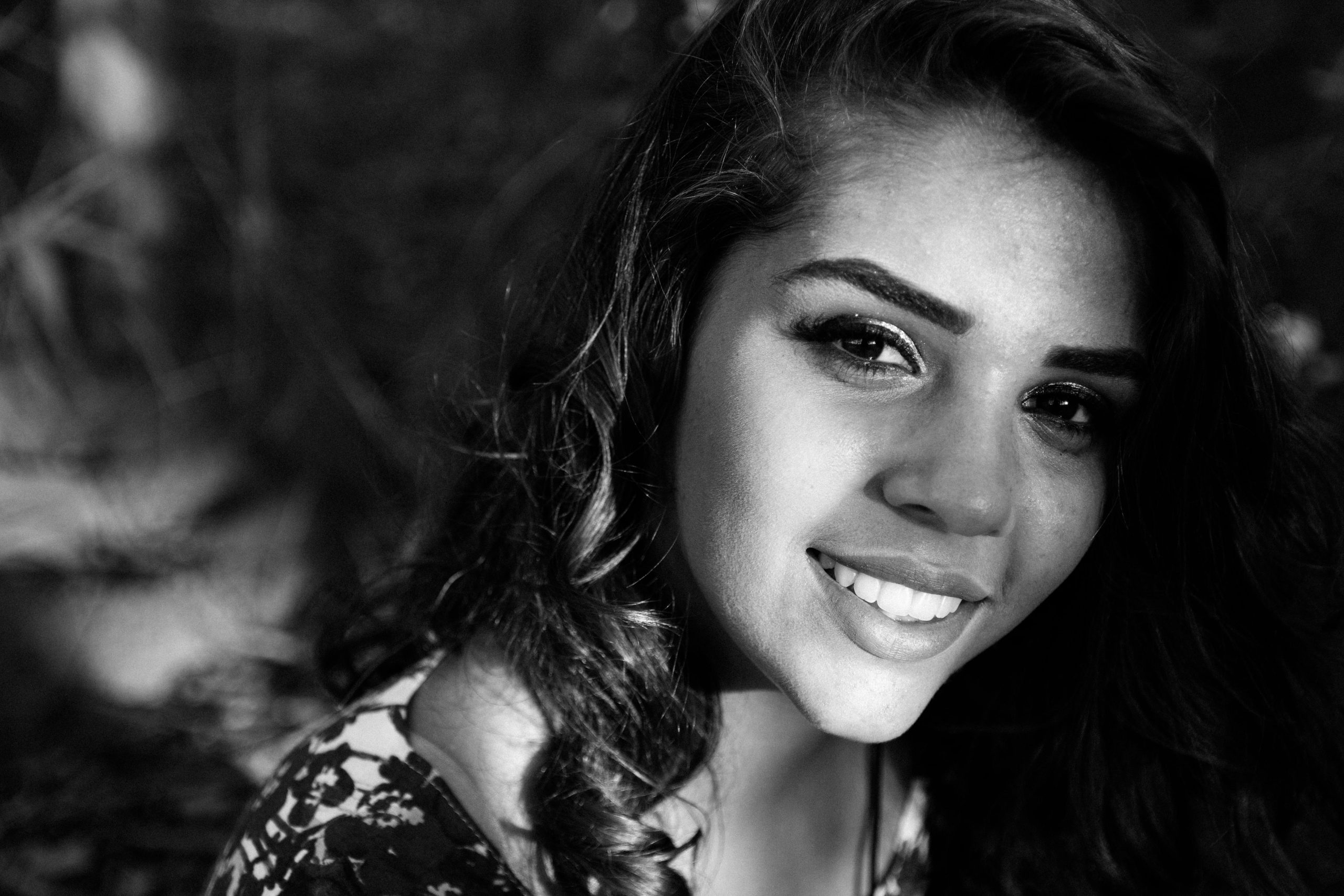 Close-up black and white portrait of a smiling Latina woman exuding elegance and charm.